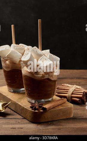 Deux verres de chocolat chaud avec des guimauves moelleuses et une paille sur un plateau en bois. Une boisson d'hiver confortable sur un fond sombre. Banque D'Images