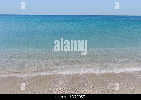 De douces vagues se glissent contre une plage de sable sous un ciel dégagé, révélant une eau cristalline Banque D'Images