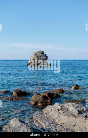 Une vue sereine sur une île rocheuse entourée d'eaux bleues calmes sous un ciel clair Banque D'Images