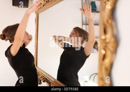 Femme dansant en toute confiance devant un grand miroir orné, mettant en valeur l'expression de soi dans un cadre élégant Banque D'Images
