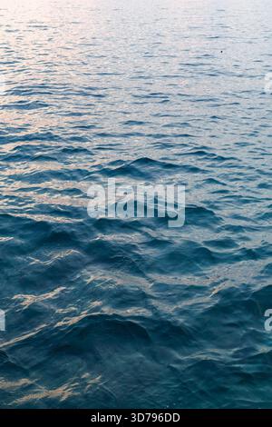 Les vagues sereines se tapissent doucement contre le rivage lors d'une soirée calme, reflétant les couleurs douces du coucher de soleil Banque D'Images