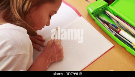 Fille chinoise penchée dans le dessin de tee-shirt blanc dans le carnet ligné au bureau, étui vert tenant un crayon pâle Banque D'Images