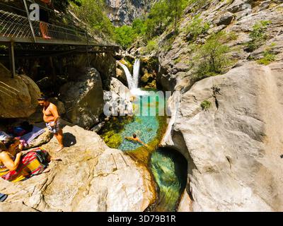 Alanya, Turquie - 13 juin 2024 : touristes se relaxant sur de grands rochers à côté d'une piscine turquoise cristalline et petite cascade dans une gorge ombragée. Les gens Banque D'Images