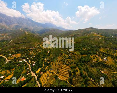 Vue aérienne panoramique d'un vaste paysage montagneux ensoleillé avec des parcelles agricoles en terrasses et une petite communauté nichée dans la vallée Banque D'Images