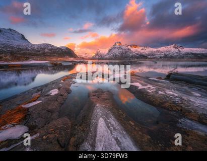 Montagnes enneigées reflétant sur le lac calme avec des pierres au lever du soleil Banque D'Images