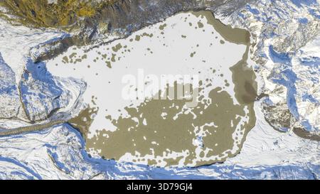 Vue aérienne d'une lagune glaciaire partiellement gelée, sa surface glacée marbrée de sédiments et entourée d'un terrain poussiéreux de neige, Fjallsarlon, Sveitarfel Banque D'Images