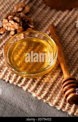 Miel d'acacia dans un bol en verre avec des noix et une trempette de miel en bois Banque D'Images