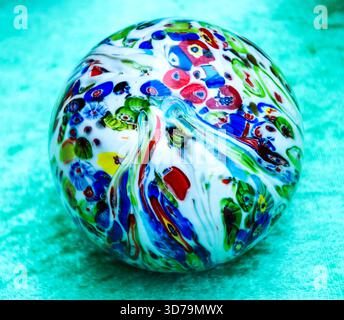 Boule de marbre en verre coloré isolée sur fond de velours turquoise. Banque D'Images