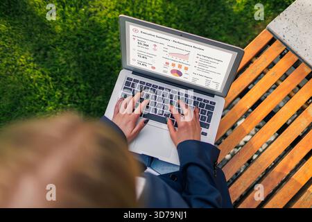vue de dessus d'une jeune femme travaillant sur un ordinateur portable dans un banc de parc tout en examinant les données Banque D'Images