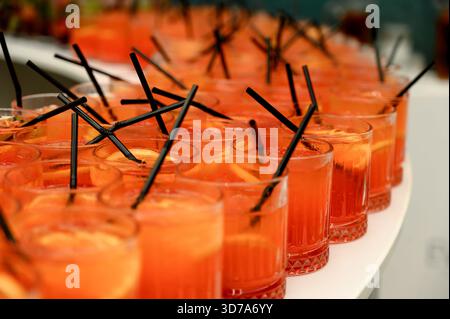 Beaucoup de cocktails orange avec des pailles orange et noires au buffet.Close-up de cocktails orange vif sur une table blanche. Banque D'Images