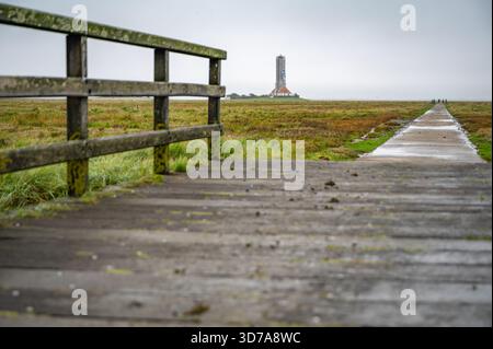 Une passerelle en bois altérée mène au site de construction du phare de Westerhever dans un champ herbeux, avec quelques personnes visibles au loin, mer du Nord, Banque D'Images
