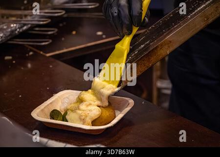 Fromage à raclette fondu glissant d'une poêle chaude sur des pommes de terre bouillies, spécialité suisse, étal de restaurant à fondue, marché de Noël de Zurich en Suisse Banque D'Images
