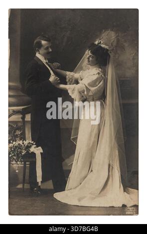 Une mariée souriante dans un long voile et robe de mariée tient doucement la main de son marié, qui est habillé d'un costume, dans un plan de studio posé. Banque D'Images