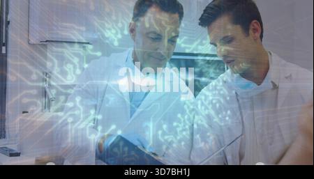 Examen de deux cliniciens pointant la tablette dans la salle d'examen en blouses de laboratoire et masques, superposition numérique Banque D'Images