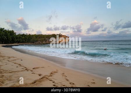 Une surfeuse solitaire pagaie à Shipwreck Beach près de Makawehi point à la fin de la journée. Banque D'Images