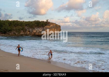 Deux femmes arrivent avec leur planche à Shipwreck Beach près de Makawehi point à la fin de la journée. Banque D'Images