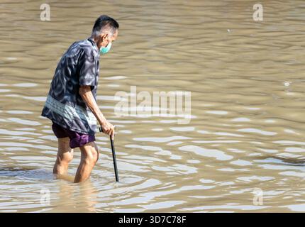 BANGKOK, THAÏLANDE, nov 09 2025, un homme âgé avec un bâton de marche patère soigneusement dans une rue inondée Banque D'Images