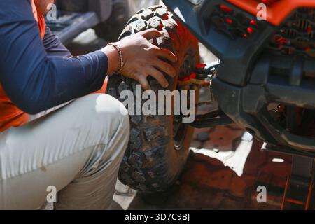 Mécanicien concentré sur la vérification des pneus robustes sur un véhicule tout-terrain pendant la course. Homme en action réparant la roue avec concentration, montrant les mains sur le maintenan Banque D'Images