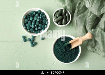 Bols de poudre de spiruline avec des capsules et des comprimés sur fond de bois vert Banque D'Images