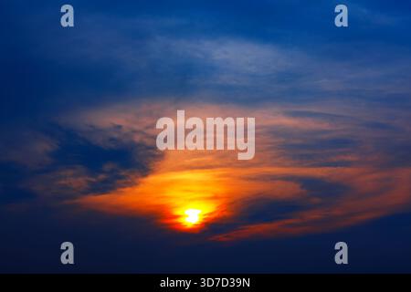 Le ciel brille de teintes orange et dorées tandis que le soleil jette un œil à travers les nuages dispersés, projetant une lumière spectaculaire à travers l'horizon. Couronne dégradé bleu profond Banque D'Images