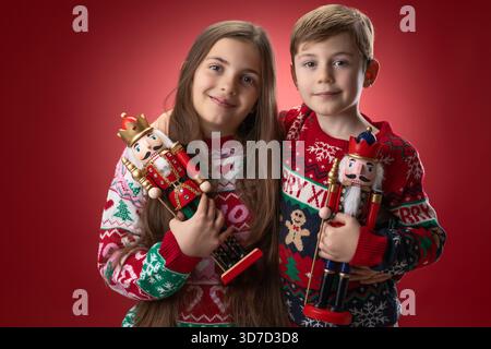 Joyeux enfants garçon et fille dans les chandails de Noël festifs tiennent des figures de jouet casse-noisette pour Happy Holiday photo, la Saint-Sylvestre et le temps de la famille Banque D'Images
