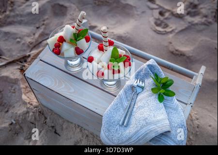 Salade de fruits saine avec framboises melon et menthe servie dans des tasses en verre à l'extérieur sur la plage de sable. Banque D'Images