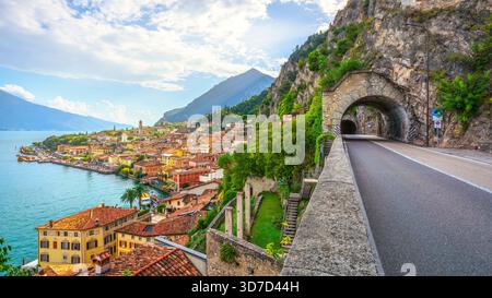 Vue sur la route enserrant la falaise rocheuse au-dessus du lac de Garde, avec une entrée de tunnel en pierre. Le village pittoresque de Limone sul Garda est visi Banque D'Images