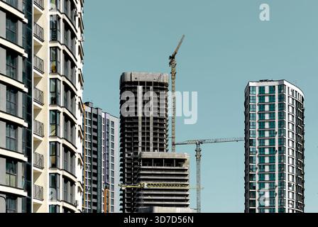Architecture d'immeubles modernes de grande hauteur avec façades en verre et grues près de la tour inachevée. Horizon urbain avec des tours de logements résidentiels Banque D'Images