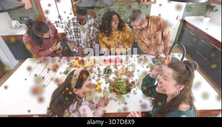 Hacher six adultes préparant un repas à l'îlot de cuisine, à l'aide de planches à découper et d'un couteau de chef. Cuisine, groupe, amis, occasionnel, maison, moderne, travail d'équipe Banque D'Images