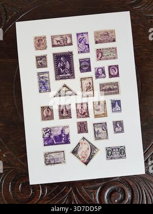 Une feuille de timbres-poste violets vintage du monde entier sur une table en chêne sculpté. Banque D'Images