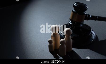 Un marteau en bois à côté d'un groupe de quatre poupées en bois. Droit de la famille, justice juridique, garde des enfants, politique sociale et concept de protection de la famille. Banque D'Images