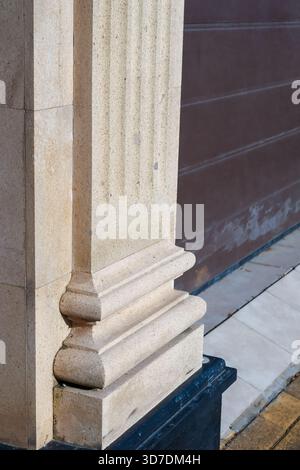 Grand pilastre cannelé de pierre pâle à côté d'une porte de garage brune, montrant une altération subtile sur la chaussée carrelée ci-dessous Banque D'Images
