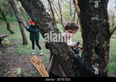 L'homme ajuste la sangle du sac à dos dans un parc pendant que l'ami prépare l'équipement sous les arbres Banque D'Images