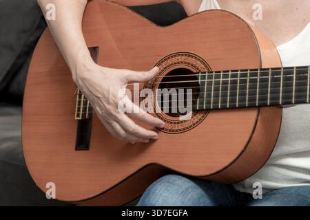 Mains de femme pincant des cordes sur une guitare acoustique classique, créant de la musique Banque D'Images