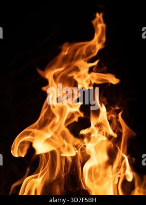 Feu capturé sur fond noir avec des languettes de flamme tordues et spirales vers le haut contre l'obscurité, créant des formes fluides qui évoquent le mouvement et le tr Banque D'Images