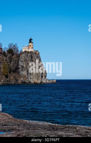 Une image orientée portrait du phare de Split Rock au sommet d'une falaise rocheuse, et de l'eau d'une petite flaque d'eau et du lac supérieur massif reflétant le cercle Banque D'Images