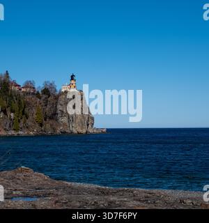 Une image carrée du phare de Split Rock au sommet d'une falaise rocheuse, et l'eau d'une petite flaque d'eau et le lac supérieur massif reflétant le ciel bleu, sur un Banque D'Images