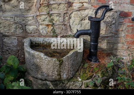 Pompe à eau manuelle à l'ancienne avec bassin en pierre dans une cour de ferme utilisée pour tirer l'eau d'un puits souterrain ou d'une source d'eau Banque D'Images