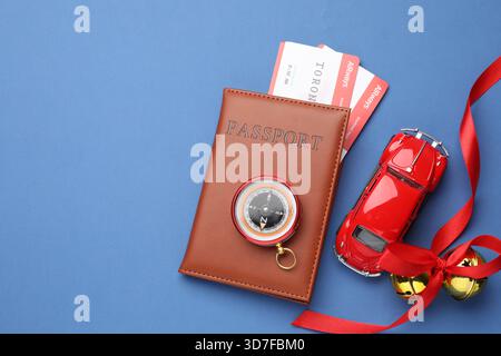 Vacances de Noël. Passeport avec billets, voiture jouet, boussole et cloches de jingle sur fond bleu, plat. Espace pour le texte Banque D'Images
