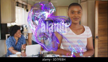 Femme debout en rose-tee serrant dans la cuisine avec ordinateur portable, tasses et hologramme violet, espace de copie Banque D'Images