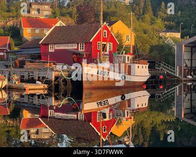 Bateau de pêche traditionnel et hangar à bateaux rouge reflété dans l'eau calme du matin du port de Sagvåg sur l'île de Stord, en Norvège Banque D'Images