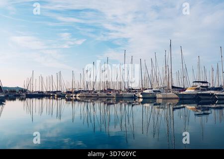 Marina calme avec des bateaux à voile réfléchis au lever du soleil Banque D'Images