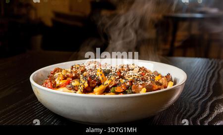 Fumer de l'udon de bœuf chaud avec du brocoli, des oignons et des poivrons dans un beau bol. Bouillon riche, légumes frais, parfait pour la cuisine japonaise. Banque D'Images