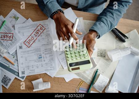 Jeune homme noir analysant les factures et les factures à l'aide de la calculatrice au bureau Banque D'Images