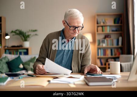 Homme principal analysant les factures des ménages et utilisant la calculatrice au bureau Banque D'Images