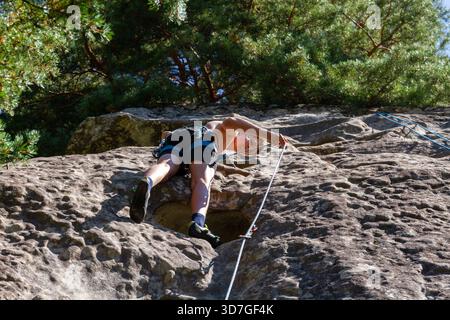 Jeune homme grimpant sur une falaise extérieure, portant un casque et un harnais, montant soigneusement la paroi rocheuse naturelle par une journée ensoleillée. Banque D'Images