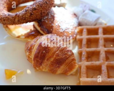 Un appétissant plateau de petit déjeuner avec un croissant feuilleté, des gaufres dorées et une pâtisserie de bague de sésame sur une assiette blanche. Parfait pour les repas du matin Banque D'Images