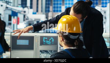 Directeur d'usine de fabrication de panneaux solaires montrant à l'ingénieur sur PC comment développer des prototypes pour de nouveaux systèmes d'énergie solaire. Chef d'équipe informant le technicien des nouveaux matériaux photovoltaïques, caméra B. Banque D'Images