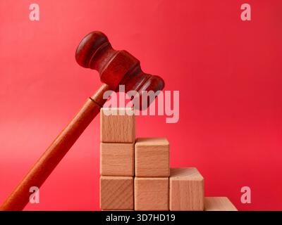L'image montre un marteau en bois à côté d'une pile de cubes en bois sur un fond rouge. Banque D'Images