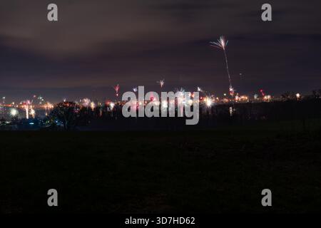 Spectacle spectaculaire de feux d'artifice colorés répartis dans le ciel au-dessus d'une ville lointaine la veille du nouvel an, avec un grand sentier d'éclatement pour une effe spectaculaire Banque D'Images